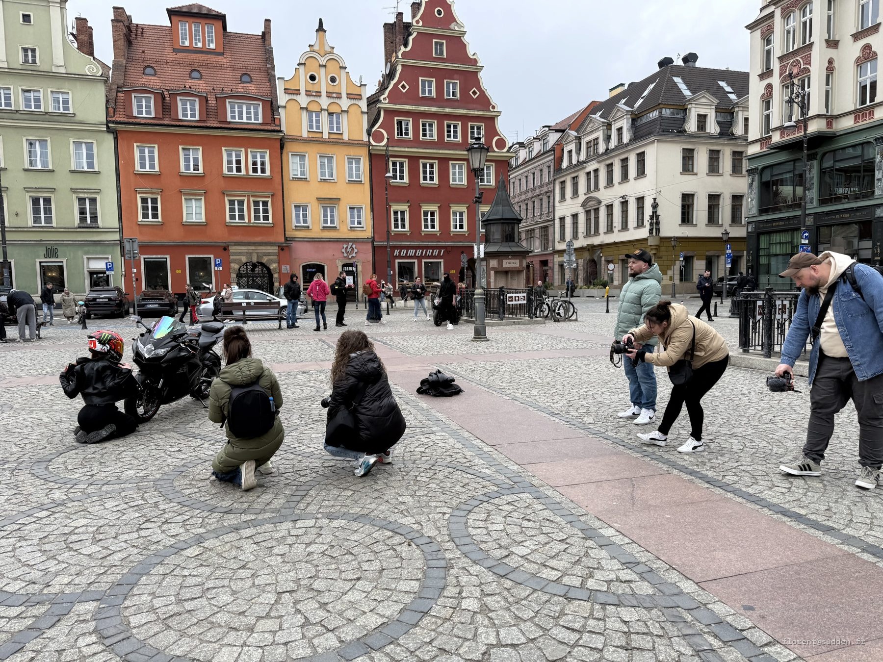 Façades gothiques colorées de la place du marché de Wrocław, avec une moto photographiée par des passants