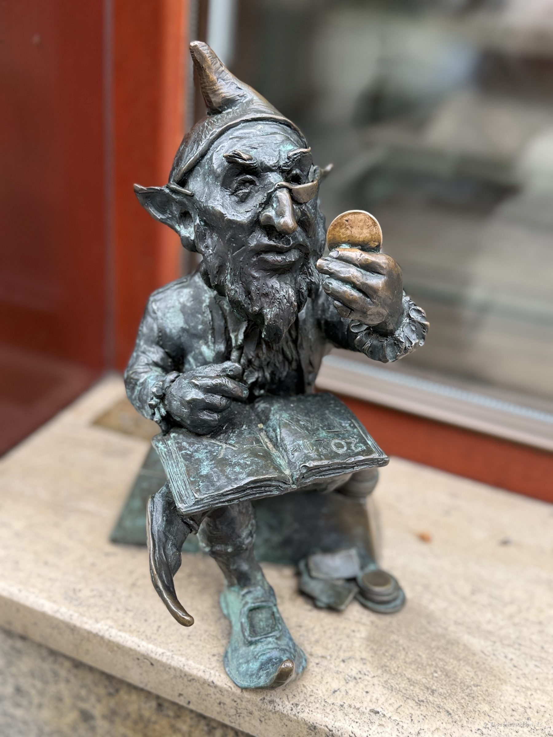 Statue de nain de bronze lisant un livre et tenant une pièce, l'une des figurines emblématiques de Wrocław