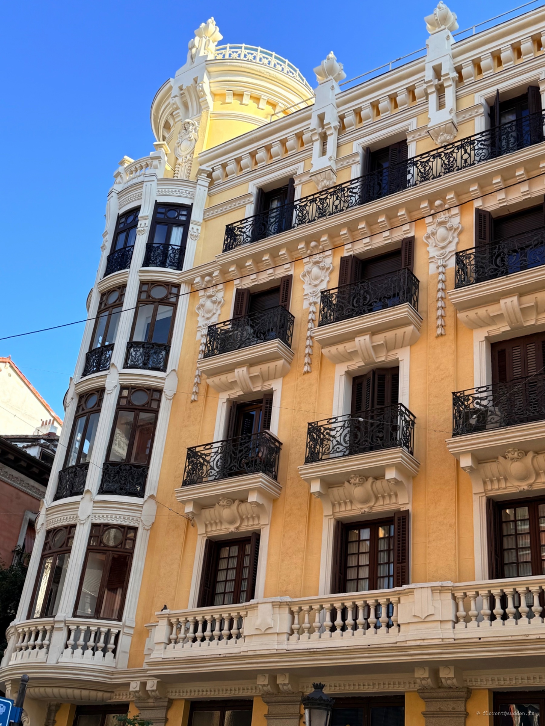 Façade jaune : Balcons noirs, fer forgé en boucle.